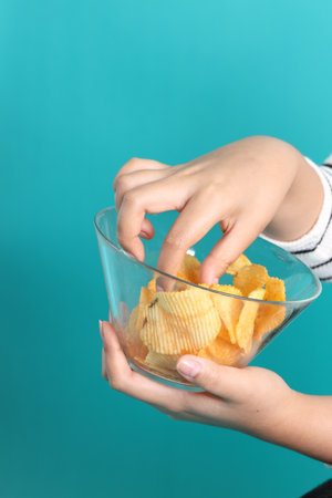 The Asian woman holding potato chips in the hand on the yellow background.の写真素材