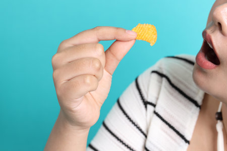 The Asian woman eating potato chips from the hand on the yellow background.