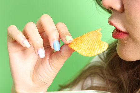 The Asian woman eating potato chips from the hand on the green background.の写真素材