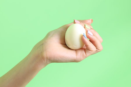 The Asian woman holding egg in the hand on the green background.