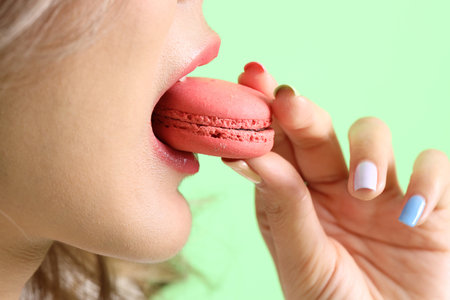 The Asian woman eating macaroons from the hand on the yellow background.の素材 [FY310213909974]