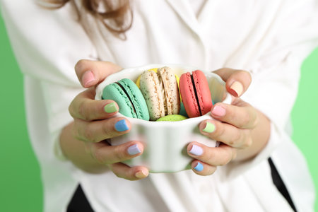 The Asian woman holding macaroons in the hand on the yellow background.の写真素材