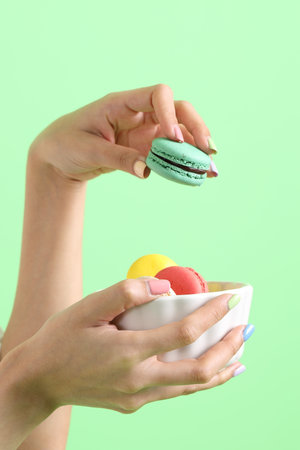 The Asian woman holding macaroons in the hand on the yellow background.