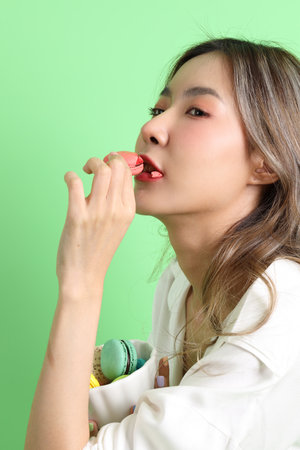 The Asian woman eating macaroons from the hand on the yellow background.の写真素材