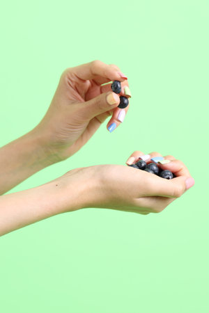 The Asian woman holding berry fruit in the hand on the yellow background.