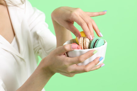 The Asian woman holding macaroons in the hand on the yellow background.の写真素材