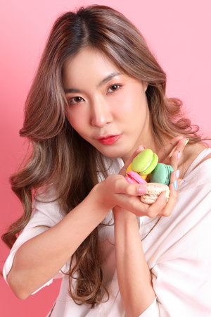 The Asian woman holding macaroons in the hand on the pink background.の写真素材