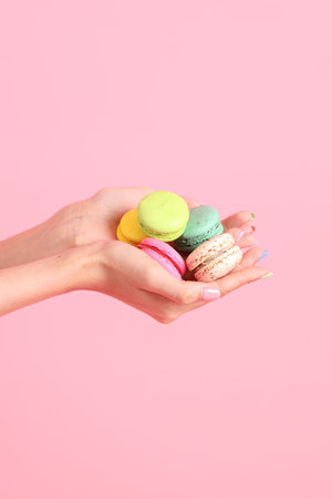 The Asian woman holding macaroons in the hand on the pink background.の写真素材