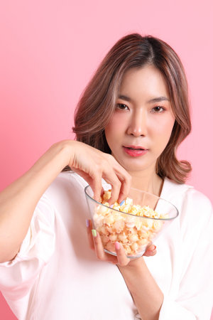 The Asian woman holding popcorn in the hand on the pink background.の写真素材