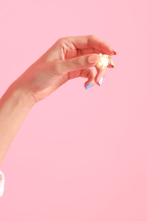 The Asian woman holding popcorn in the hand on the pink background.