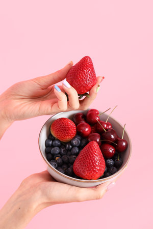 The Asian woman holding berry fruit in the hand on the pink background.の写真素材
