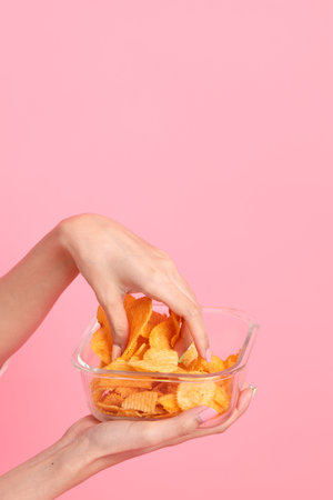 The Asian woman eating potato chips from the hand on the pink background.の写真素材