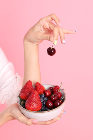 The Asian woman holding berry fruit in the hand on the pink background.の写真素材