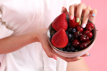 The Asian woman holding berry fruit in the hand on the pink background.