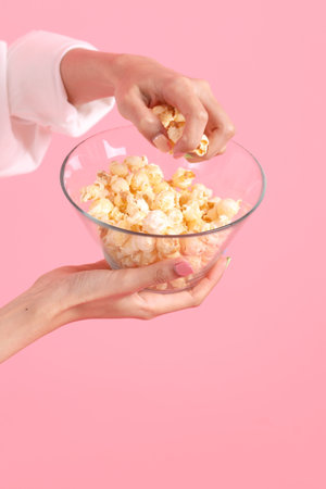 The Asian woman holding popcorn in the hand on the pink background.の写真素材