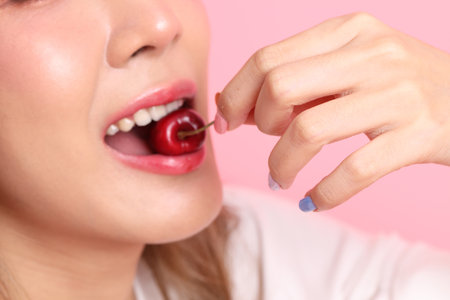 The Asian woman eating fruit from the hand on the pink background.