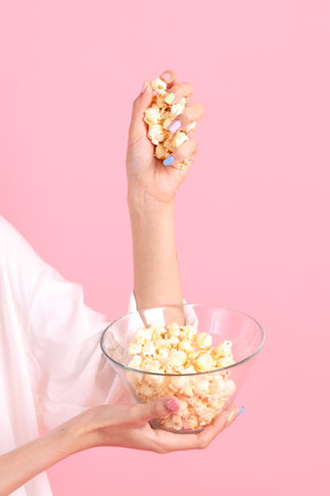 The Asian woman holding popcorn in the hand on the pink background.の写真素材