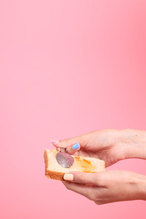 The Asian woman filling the orange jam to the sliced bread  in the pink background.