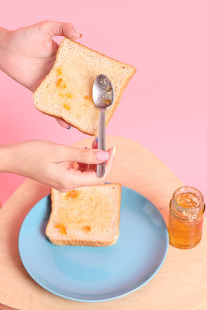 The Asian woman filling the orange jam to the sliced bread  in the pink background.の写真素材