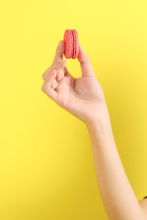 The Asian woman eating macaroons from the hand on the yellow background.の写真素材