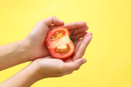 The Asian woman holding tomato on the yellow background.の写真素材