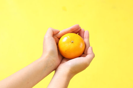 The Asian woman holding orange fruit on the yellow background.の写真素材