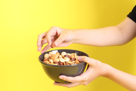 The Asian woman holding nuts on the yellow background.の写真素材