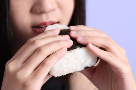 The Asian woman eating onigiri from the hand on the purple background.の写真素材