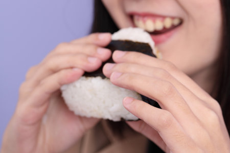 The Asian woman eating onigiri from the hand on the purple background.の写真素材