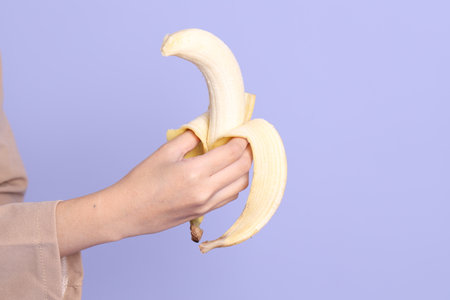 The Asian woman eating banana from the hand on the purple background.の写真素材