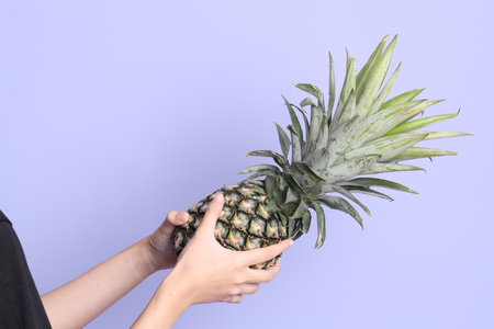 The Asian woman hand holding pineapple in the purple background.の写真素材