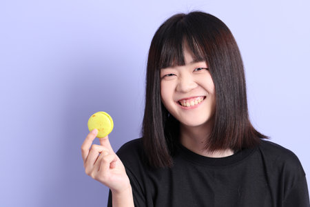 The Asian woman holding macaroon on the purple background.の写真素材