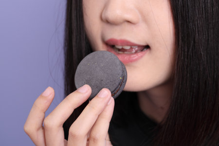 The Asian woman holding macaroon on the purple background.の写真素材
