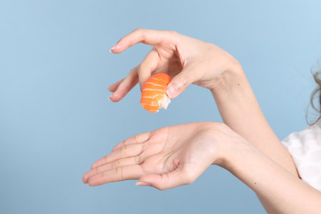 The Asian woman hand holding sushi in the blue background.
