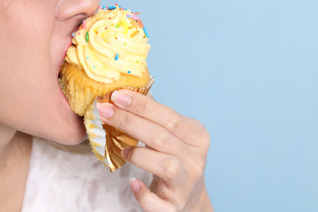The Asian woman eating cupcakes on the blue background.の写真素材