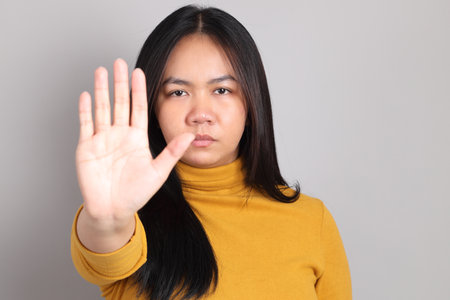 The adult Southeast Asian woman standing on the grey showing hand sign.