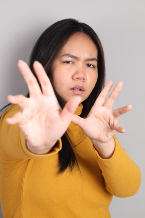The adult Southeast Asian woman standing on the grey showing hand sign.