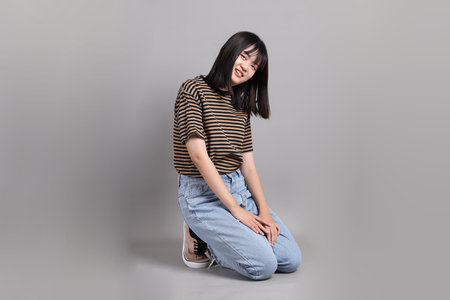 The full length of young adult Asian woman sitting on the grey background.