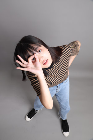 The full length of young adult Asian woman standing on the grey background.の写真素材