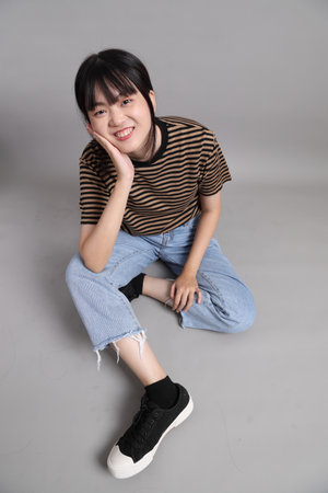 The full length of young adult Asian woman standing on the grey background.