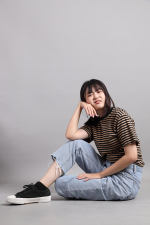 The full length of young adult Asian woman sitting on the grey background.の写真素材