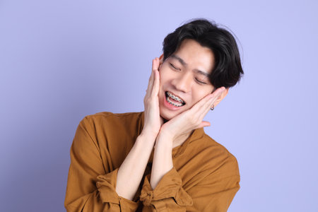The Adult east Asian man with braces standing on the blue background.