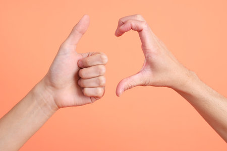 The two hand of Asian man connected each other with heart sign and thumb up sign on the pink background.の写真素材