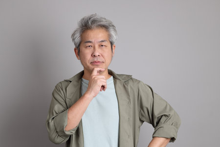 The 40s Asian man with smart casual clothes standing on the grey background.