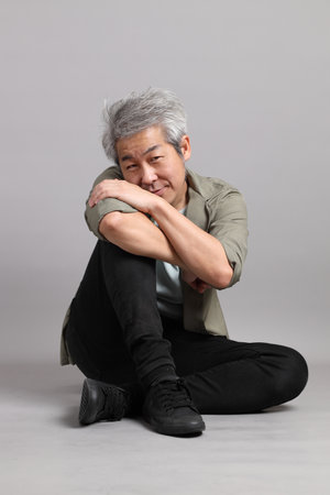 The 40s Asian man with smart casual clothes sitting on the grey background.の写真素材