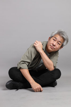 The 40s Asian man with smart casual clothes sitting on the grey background.の写真素材