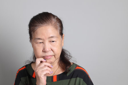 The 70s Chinese senior woman with casual clothes standing on the grey background.の写真素材