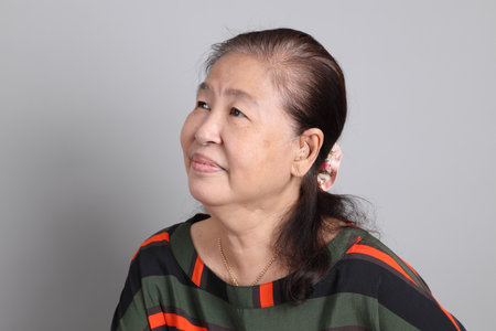 The 70s Chinese senior woman with casual clothes standing on the grey background.の写真素材