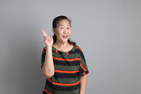 The 70s Chinese senior woman with casual clothes standing on the grey background.の写真素材