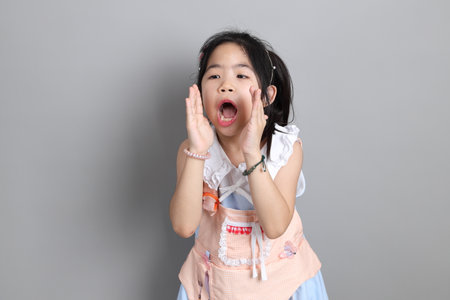The little cut Asian girl with fancy dressed standing on the grey background.